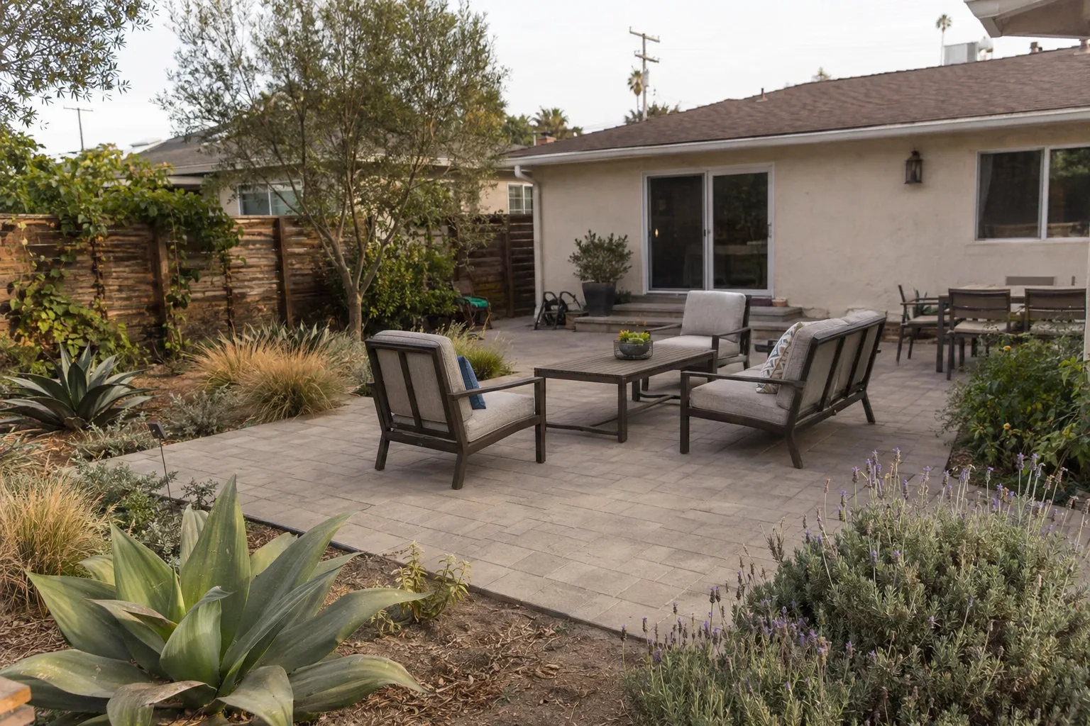 A finished concrete paver patio with outdoor seating in a Los Angeles backyard surrounded by drought-tolerant plants, bathed in late-afternoon golden light