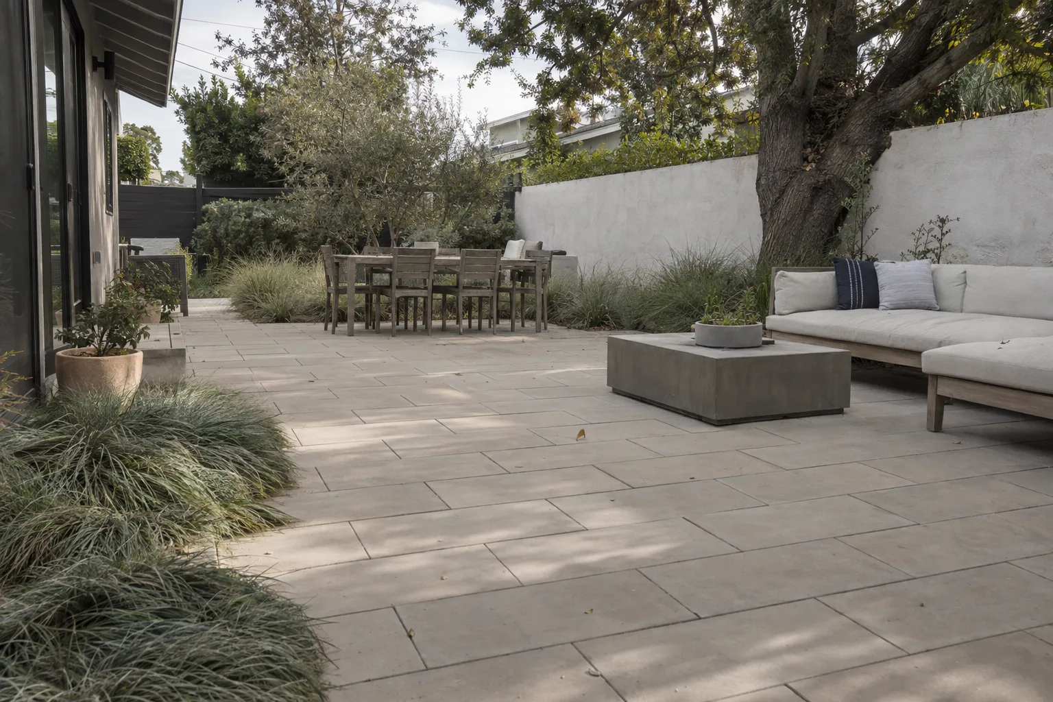 A finished concrete-paver backyard patio bordered by ornamental grasses and a stucco wall in warm late-afternoon sunlight