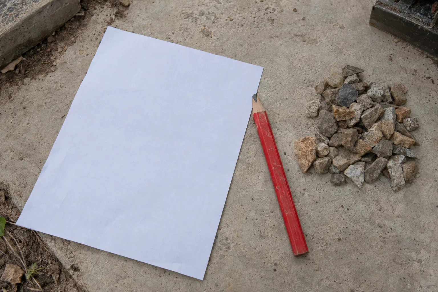 A flat-lay overhead shot of a blank cost estimate sheet, a carpenter's pencil, and small gravel samples on a light concrete surface.