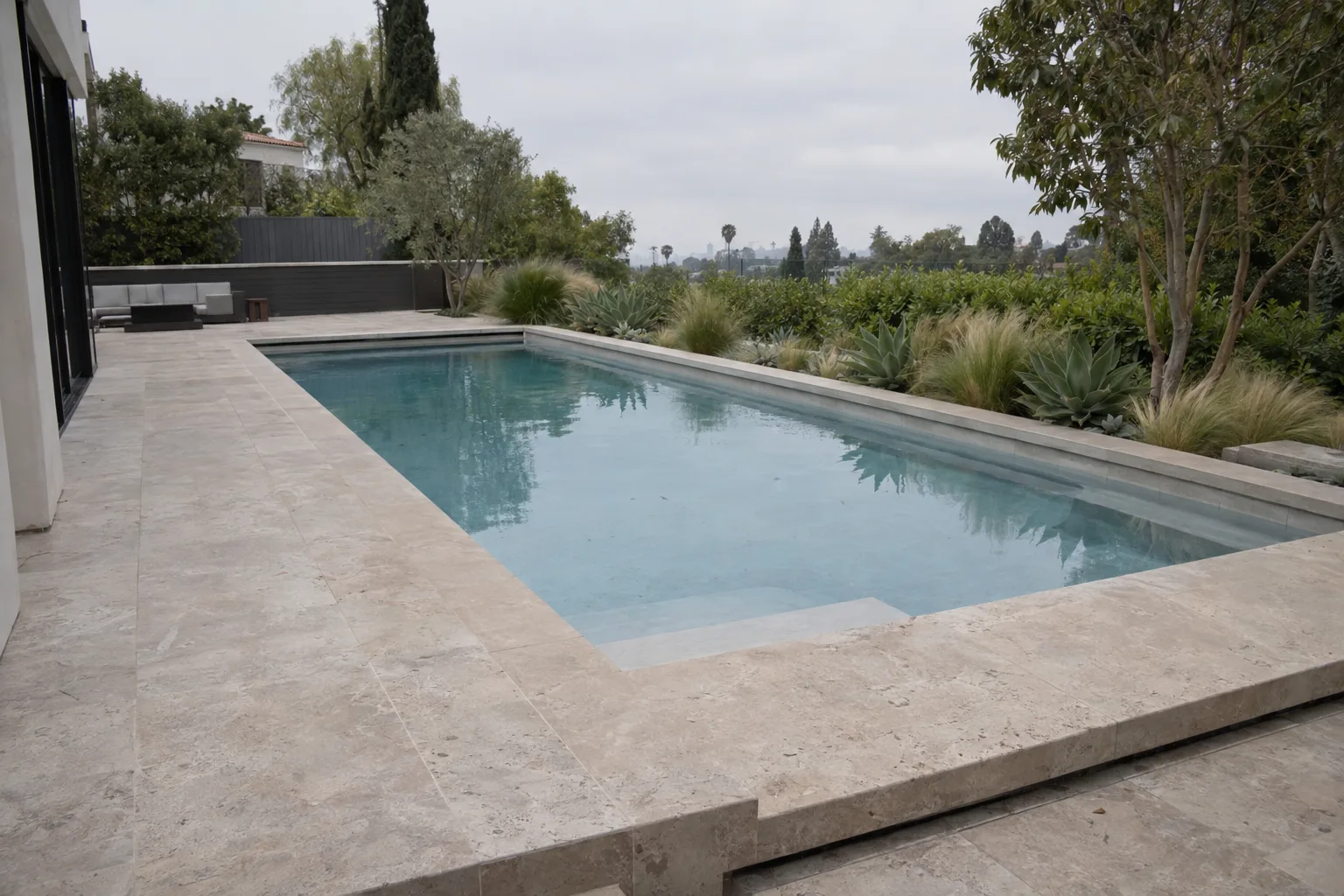 A finished rectangular pool with cantilevered travertine decking, succulent border plantings, and concrete coping at a Los Angeles residential property in late-afternoon sunlight
